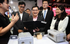 A group of professionals, including a man holding a folder and smiling, engaged in a lively discussion at a technology showcase event.